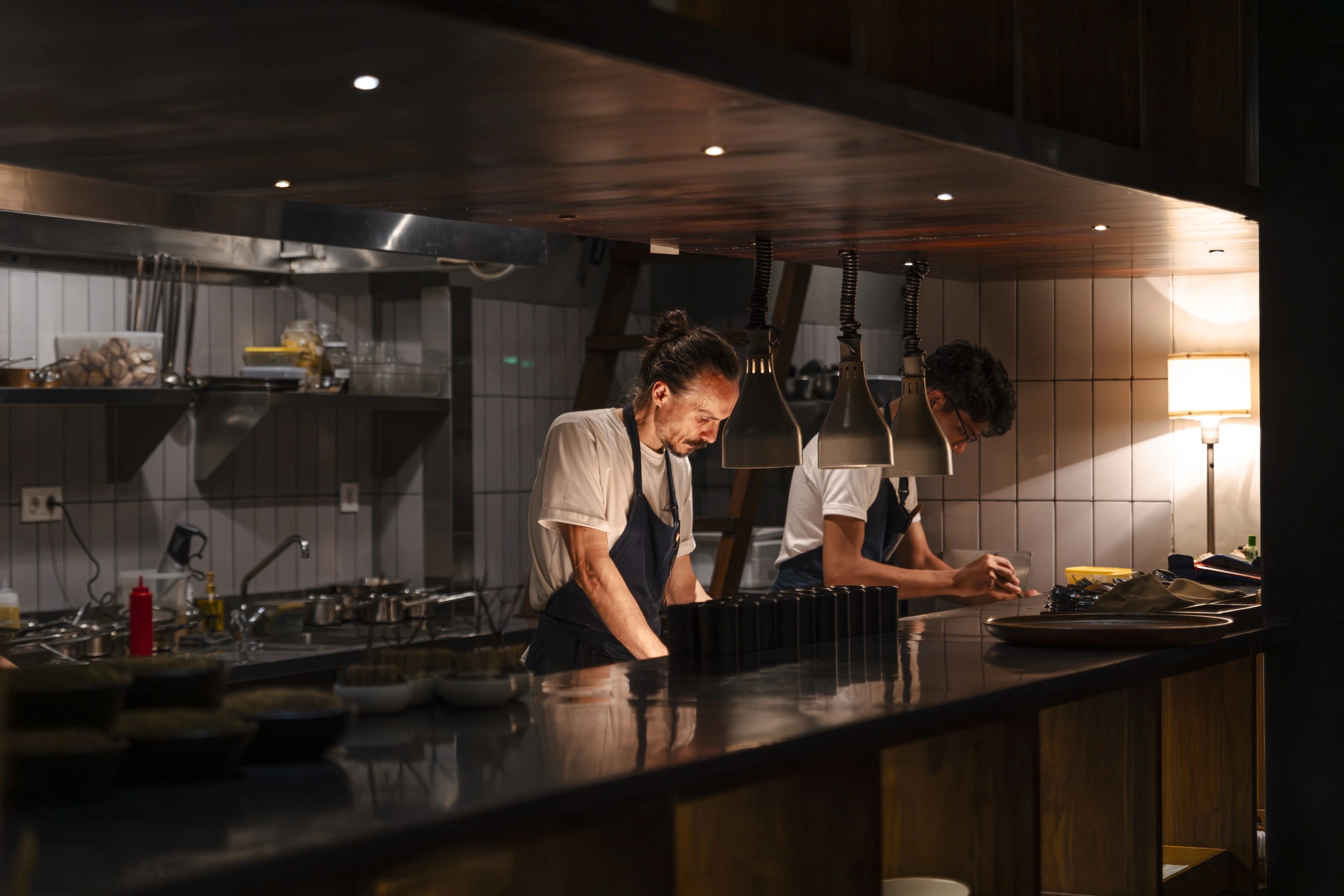 Two chefs working the pass under heat lamps during evening service at Herbivore