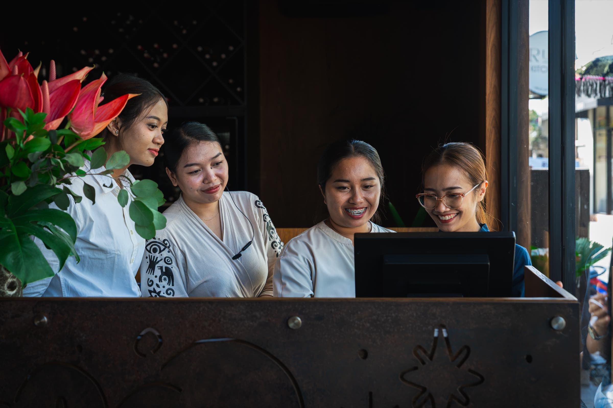 Four front-of-house staff at an Empat Group venue, gathered around the host stand screen